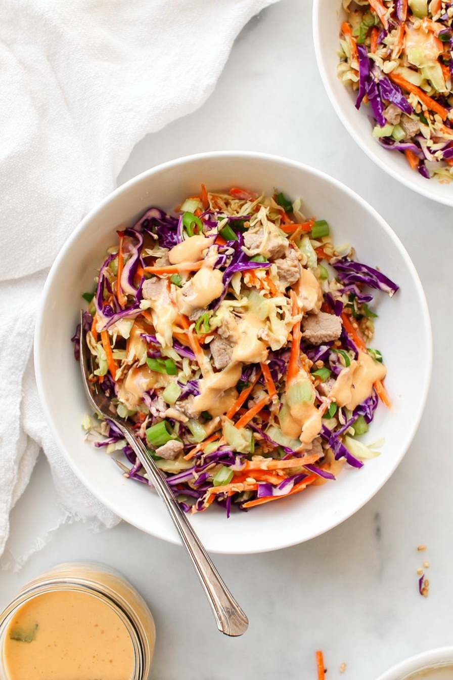 The image shows two white bowls filled with a colorful salad made of shredded purple and green cabbage, thin orange carrot strips, and small pieces of cooked light brown meat. On top of the salad is a light orange creamy dressing drizzled unevenly. The bowl in the front has a silver fork resting inside it. The background features a white marbled surface and a soft, light-colored cloth nearby. photo taken with an iphone --ar 2:3 --v 7
