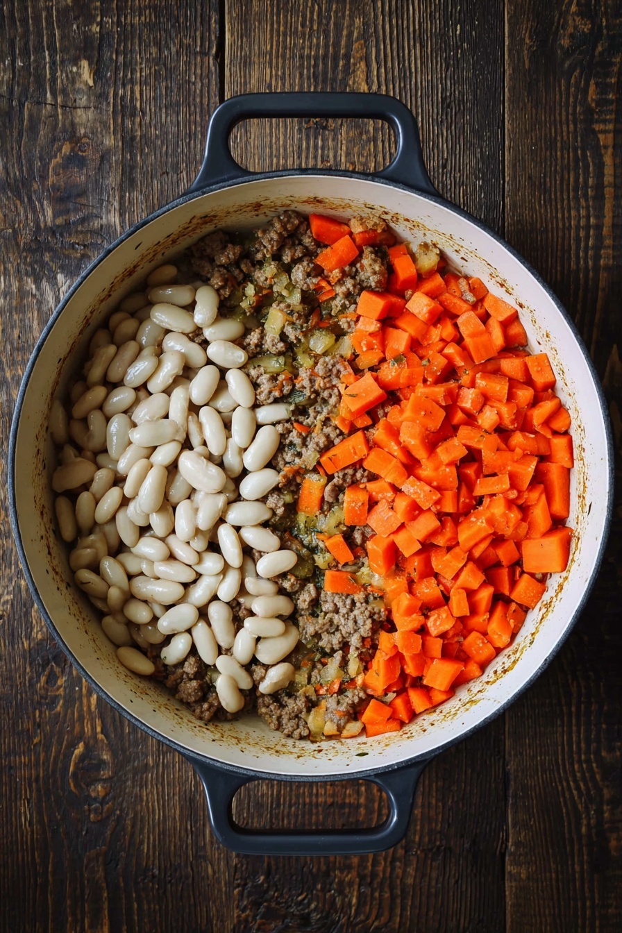 A white pot with black handles is set on a dark wooden surface, filled with three distinct layers of ingredients. The bottom layer consists of browned ground meat mixed with sautéed onions and herbs, forming a textured, brownish base with small bits scattered around. On top of this base, the right half holds bright orange carrot pieces cut into small chunks, adding a vibrant splash of color. The left half of the pot is filled with plump white beans, smooth and shiny, contrasting with the rough texture of the meat and carrots. photo taken with an iphone --ar 2:3 --v 7