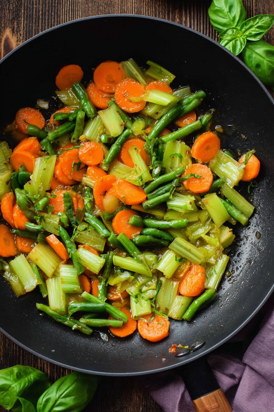 A black pan filled with a thick tomato broth soup that has three main layers visible: the bright red liquid base, mixed with small beige elbow pasta pieces scattered throughout, bright orange carrot slices shaped like small rounds, and dark green curly kale leaves that float on top. Small green beans pieces and light green celery bits are also mixed in, adding texture and color contrast. The pan rests on a dark wooden surface with some fresh green basil leaves placed nearby and a light purple cloth partially visible on the lower right. photo taken with an iphone --ar 2:3 --v 7
