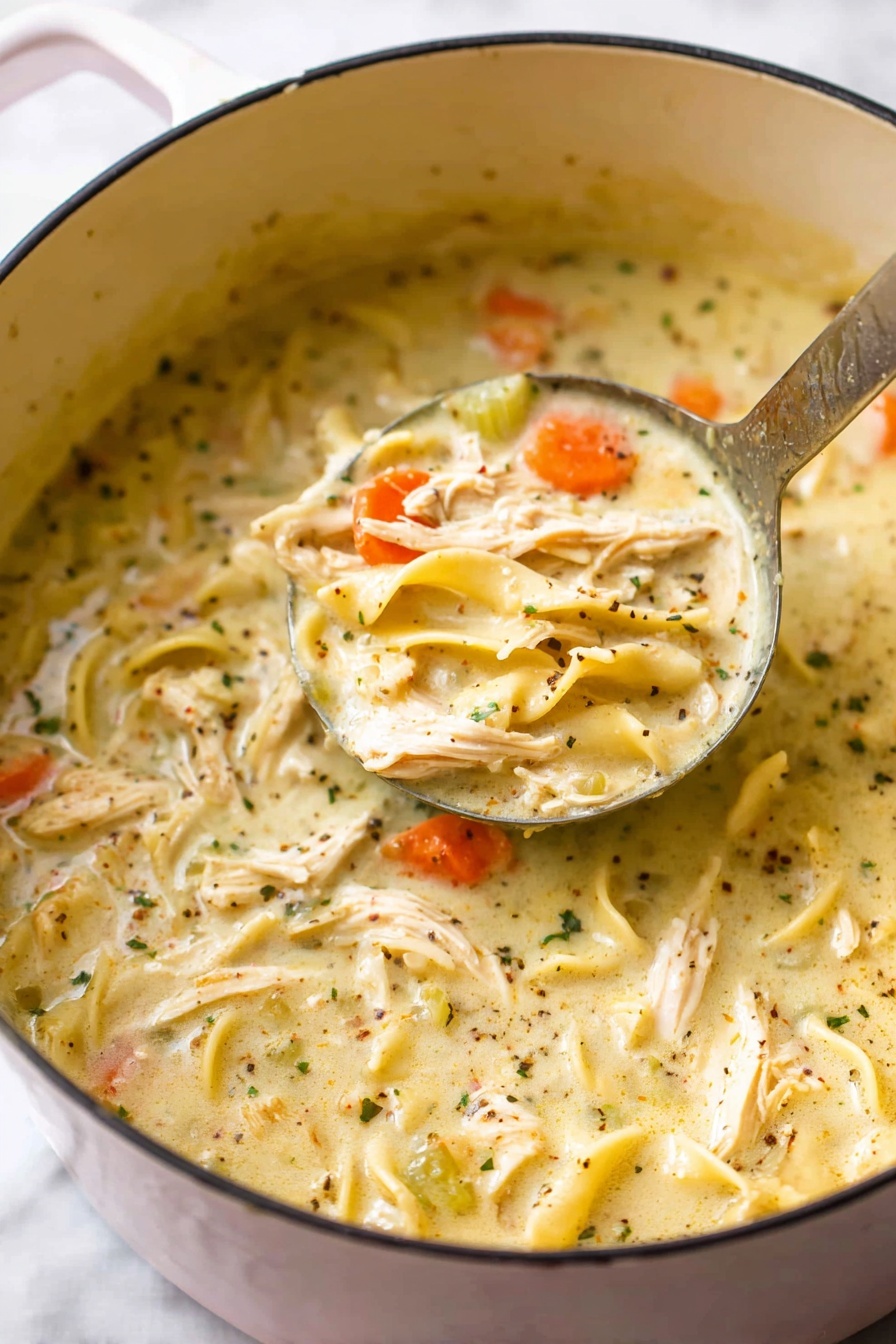 A close-up shot of a white-lined pot filled with thick, creamy chicken noodle soup. The soup has several layers including shredded chicken pieces that are beige and tender, soft yellowish noodles, bright orange carrot slices, and small bits of celery in light green. The creamy broth is pale yellow with specks of black pepper and herbs, creating a textured surface. A metal ladle is scooping some soup, showing all these layers mixed together in the ladle. The pot is placed on a white marbled surface, photo taken with an iphone --ar 2:3 --v 7